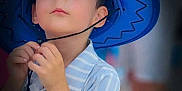 Nohlan participe au concours pour gagner de l'argent avec cette photo : child, boy, hat, cowboy_hat, blue_hat, striped_shirt, portrait, face, curious, innocent, young_child, looking_up, hands, chin_strap, soft_background, close_up, casual_clothing, indoor, person, cute
