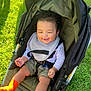 Josiah is registered to the contest to win money with this photo: baby, bib, casual_clothing, child, curly_hair, cute, grass, greenery, happy, infant, orange_socks, outdoor, person, playful, relaxed, safety_harness, smiling, stroller, sunlight, toddler