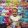 baby, bib, bracelet, brick_wall, child, clothing, colorful, happy, infant, mural, outdoor_style, photography, portrait, portrait_photography, shoes, sitting, smiling, sneakers, toy, waving