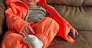 Milo joined the competition — help win amazing prizes! baby, casual_wear, child, couch, cozy, curly_hair, cute, home, indoor, infant, leather, orange_clothing, person, portrait, relaxed, sitting, socks, tracksuit, wide_eyes, young_child