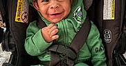 Milo joined the competition — help win amazing prizes! baby, car_seat, casual_wear, child, closeup, curly_hair, cute, expressive_face, green_clothing, happy, indoors, infant, playful, portrait, safety_harness, seated, smiling, warning_label, white_socks, young_child