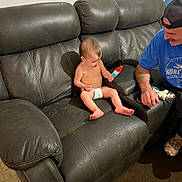 Octavia is registered to the contest to win money with this photo: toddler, child, diaper, popsicle, couch, leather, adult, man, cap, blue_shirt, smile, indoor, floor, carpet, wall_art, furniture, home, curious, person, casual