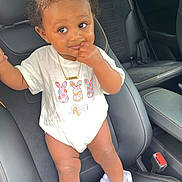 Jayciona is registered to the contest to win money with this photo: baby, bow, car_interior, car_seat, child, curly_hair, cute, expression, face, hand, indoor, jewelry, necklace, person, ruffles, seat_belt, shoes, standing, toddler, white_onesie