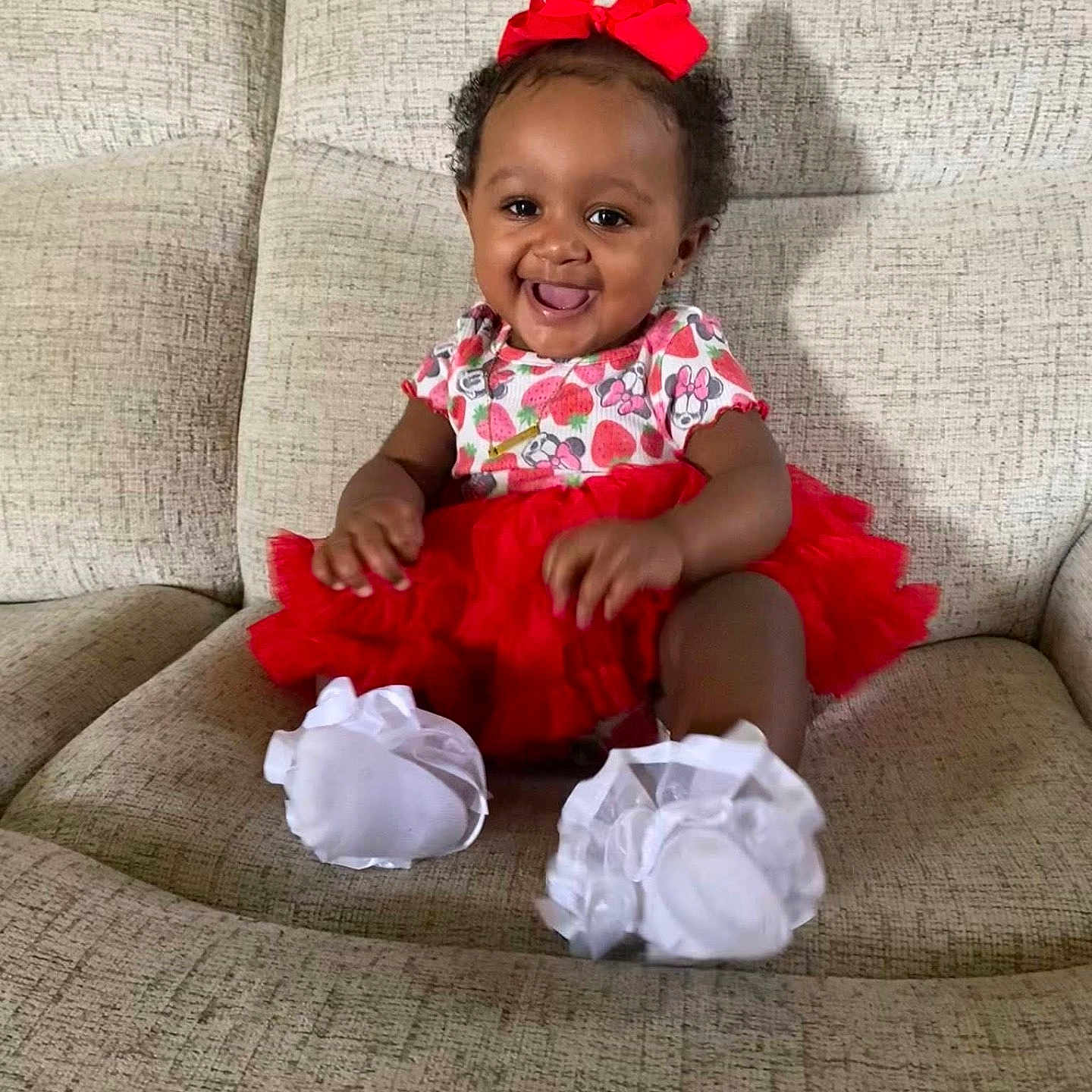 Jayciona is registered to the contest to win money with this photo: baby, child, clothing, couch, cute, face, footwear, furniture, happy, headwear, indoor, infant, person, portrait, red_bow, red_tutu, sitting, smiling, toddler, white_shoes
