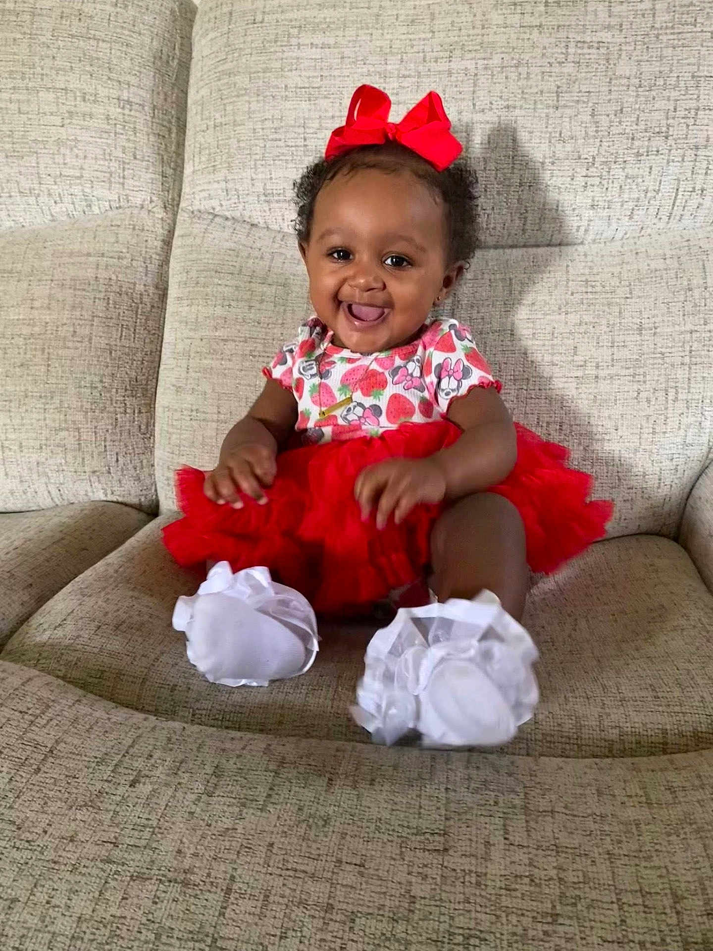 Jayciona is registered to the contest to win money with this photo: baby, child, clothing, couch, cute, face, footwear, furniture, happy, headwear, indoor, infant, person, portrait, red_bow, red_tutu, sitting, smiling, toddler, white_shoes