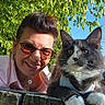 woman, cat, outdoor, greenery, blue_sky, sunglasses, hoop_earrings, smiling, fluffy_cat, wooden_surface, portrait, pet, nature, sunlight, happy, closeup, face, fur, animal, casual