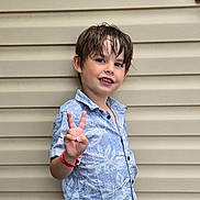 Nathan participe au concours pour gagner de l'argent avec cette photo : child, boy, peace_sign, wet_hair, blue_shirt, floral_pattern, wristband, smile, posing, standing, outdoor, beige_wall, background, casual_clothing, portrait, happy, young, person, summer, expression