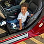 toddler, child, car, corvette, toy, smiling, curly_hair, white_shirt, jeans, sneakers, leather_seat, seatbelt, sunlight, dashboard, steering_wheel, car_interior, happy, playing, vehicle, door