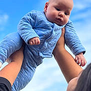 Gabriel participe au concours pour gagner de l'argent avec cette photo : baby, blue_onesie, child, sky, clouds, outdoor, person, arms, hands, cute, infant, portrait, happy, holding, face, head, fingers, warm_clothing, daylight, family