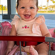 Victoria is registered to the contest to win money with this photo: baby, child, smiling, shopping_cart, blanket, pink, outdoor, daylight, happy, person, clothing, earrings, foot, seatbelt, metal, grid_floor, trees, architecture, sunlight, cute