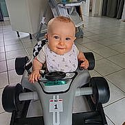 Ethan participe au concours pour gagner de l'argent avec cette photo : baby, bib, blue_eyes, child, cute, floor_tiles, furniture, hands, high_chair, home, indoor, infant, person, playful, race_car, seat, smiling, steering_wheel, toy_car, vehicle