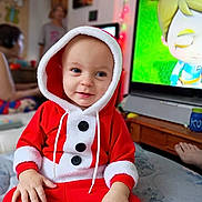 Isaiah joined the competition — help win amazing prizes! toddler, child, santa_outfit, red_clothing, hood, indoor, television, animation, bed, furniture, person, smile, happy, holiday, festive, buttons, hand, face, cozy, room