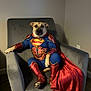 dog, superman_costume, cape, armchair, pet, indoor, costume, canine, relaxed, fur, brown, red, blue, superhero, sitting, paw, legs, ears, face, domestic_animal