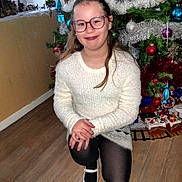 Estrella a rejoint le concours — aidez-le/la à gagner de superbes lots ! child, girl, glasses, white_sweater, black_tights, white_shoes, christmas_tree, ornaments, holiday_decorations, train_set, wooden_floor, indoor, smiling, festive, kneeled, long_hair, home, seasonal, celebration, happy