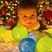 Jacob is registered to the contest to win money with this photo: baby, child, lights, christmas_tree, fireplace, stocking, gift, snow, holiday, festive, decorations, indoor, cozy, warm_lighting, colorful, smiling, face, christmas, celebration, cute