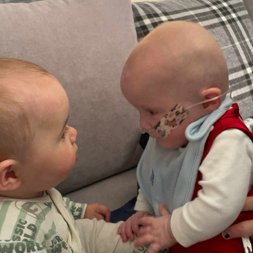 Twins joined the competition — help win amazing prizes! baby, child, clothing, couch, cute, face, hand, holding_hands, home, indoor, infant, interaction, medical_tape, nasal_tube, pattern, person, pillow, plaid, sitting, toddler