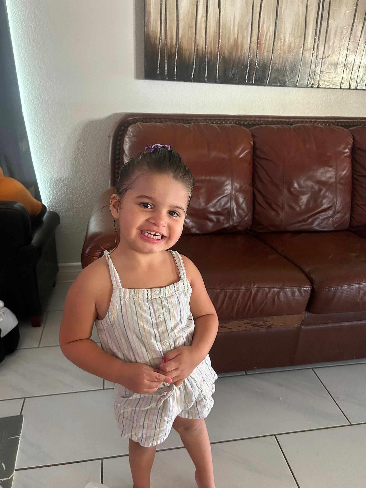 Kaya joined the competition — help win amazing prizes! child, girl, smile, happy, standing, indoor, living_room, couch, leather_couch, wall_art, tile_floor, clothing, hair_tie, person, portrait, casual, home, furniture, young_child, cute