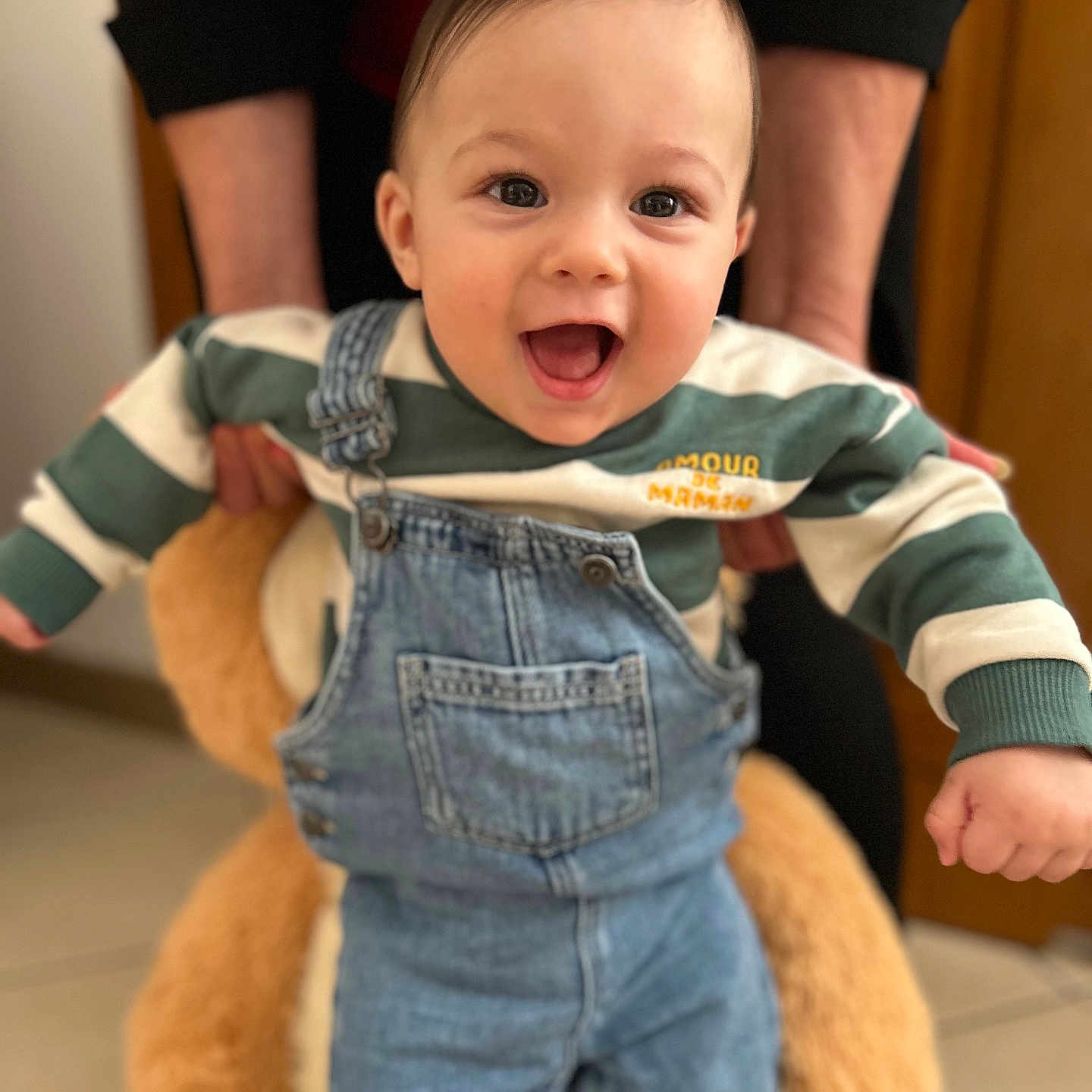 Kaïl participe au concours pour gagner de l'argent avec cette photo : baby, casual_clothing, child, cute, denim_overalls, expression, floor, furniture, hands, happy, holding, indoor, person, plush_toy, portrait, smiling, striped_sweater, support, teddy_bear, young_child