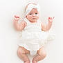 baby, infant, white_dress, headband, blue_eyes, cute, lying_down, soft_lighting, high_key, newborn, skin, barefoot, portrait, child, adorable, innocence, baby_fashion, white_background, hands_up, soft_texture