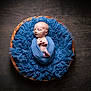newborn, baby, sleeping, wrapped, blue_cloth, blue_cushion, wicker_basket, wooden_floor, infant, peaceful, cozy, portrait, indoors, soft_texture, cute, small, resting, child, peace, baby_boy