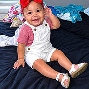 Amelia joined the competition — help win amazing prizes! baby, child, smiling, indoors, bedroom, bed, red_bow, overalls, striped_shirt, sandals, sitting, portrait, happy, infant, clothing, window, blinds, blanket, laundry, photography