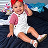 baby, child, smiling, indoors, bedroom, bed, red_bow, overalls, striped_shirt, sandals, sitting, portrait, happy, infant, clothing, window, blinds, blanket, laundry, photography