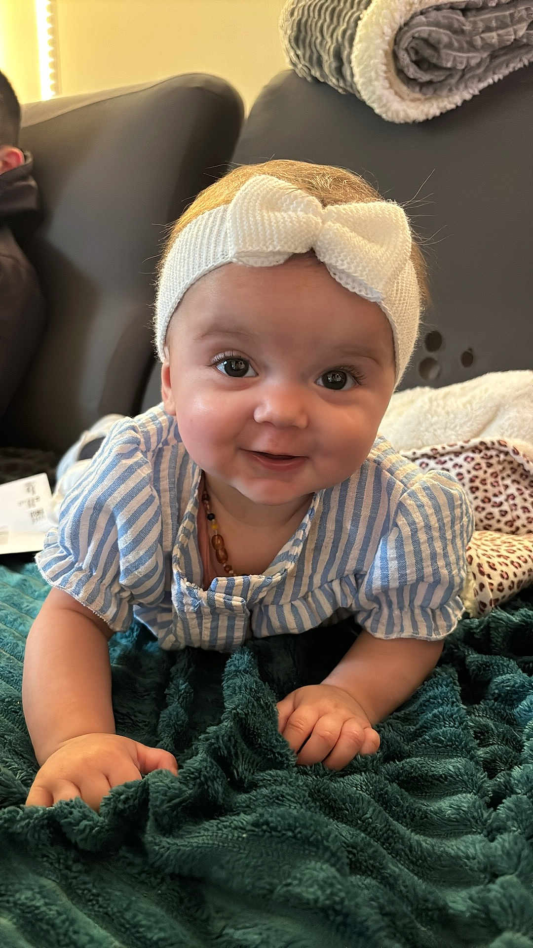 Mencïa participe au concours pour gagner de l'argent avec cette photo : baby, infant, headband, bow, smile, blanket, teal_blanket, striped_shirt, crawling, chubby_cheeks, big_eyes, necklace, couch, cozy, portrait, closeup, hand, living_room, plush, rolled_blanket