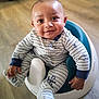 baby, child, infant, onesie, baby_seat, smiling, happy, indoor, floor, wooden_floor, cute, portrait, sitting, clothing, footwear, one_person, young_child, face, hand, looking_up