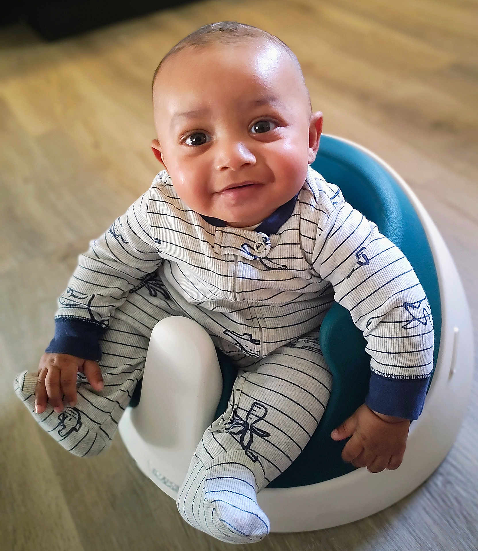 Azyias is registered to the contest to win money with this photo: baby, child, infant, onesie, baby_seat, smiling, happy, indoor, floor, wooden_floor, cute, portrait, sitting, clothing, footwear, one_person, young_child, face, hand, looking_up