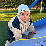 Léon Grange a rejoint le concours — aidez-le/la à gagner de superbes lots ! toddler, child, playground, slide, beanie, winter_clothes, jacket, outdoor, grass, fence, daylight, curious, climbing, blue_slide, green_background, shoes, person, young_child, casual_wear, park