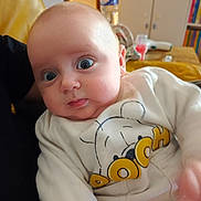 Moïse participe au concours pour gagner de l'argent avec cette photo : baby, infant, wide_eyes, surprised, onesie, winnie_the_pooh, cartoon_print, couch, indoor, water_bottle, bookshelf, nursery, close_up, portrait, soft_lighting, hand, adult_arm, rosy_cheeks, clothing, sitting