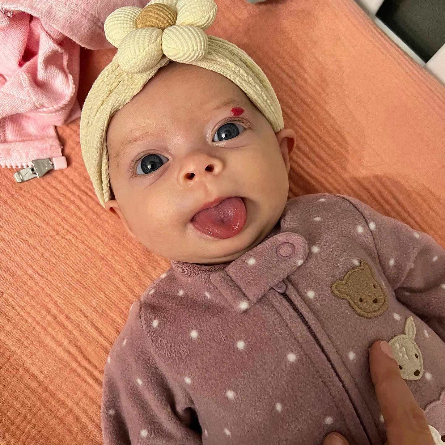 Ellanor Rose is registered to the contest to win money with this photo: baby, blanket, blue_eyes, child, cozy, cute, face, finger, flower, hand, headband, indoors, infant, lying_down, newborn, playful, polka_dots, purple_outfit, soft_texture, tongue_out