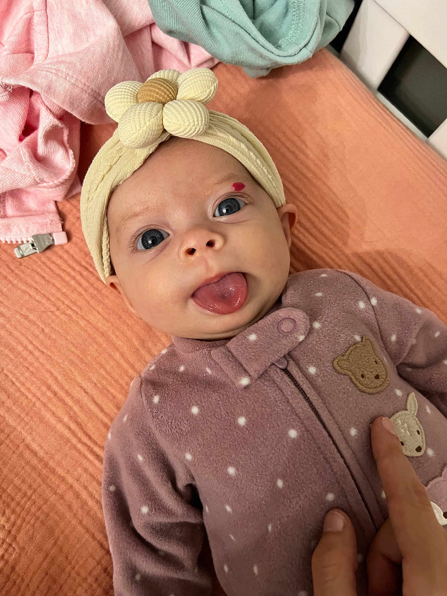 Ellanor Rose is registered to the contest to win money with this photo: baby, infant, face, tongue_out, headband, flower, purple_outfit, polka_dots, blanket, finger, hand, blue_eyes, cute, playful, lying_down, soft_texture, cozy, indoors, child, newborn