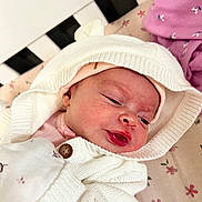 Ellanor Rose is registered to the contest to win money with this photo: baby, infant, knitted_hoodie, white_clothing, pink_clothing, blanket, floral_pattern, face, sleepy, newborn, cute, soft_texture, button, lying_down, indoors, closeup, headwear, skin, expression, child