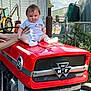 baby, child, tractor, farm, outdoor, vehicle, red, person, clothing, hand, machinery, silo, sky, cloud, grass, metal, head, expression, footwear, seat