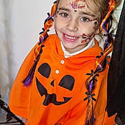 Kataleïa participe au concours pour gagner de l'argent avec cette photo : child, face_paint, halloween, costume, orange_clothing, braided_hair, smile, toy, indoor, festive, hair_ribbons, cute, happy, young, portrait, floor, black_shoes, white_wall, celebration, playful