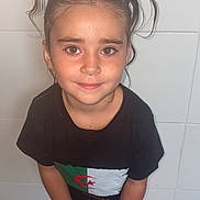 Kataleïa participe au concours pour gagner de l'argent avec cette photo : child, girl, pigtails, brown_eyes, black_tshirt, flag, pink_pajamas, standing, indoor, tile_wall, smile, cute, portrait, casual_clothing, barefoot, young, person, happy, looking_up, hair_ties