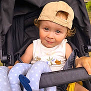 Nayan a rejoint le concours — aidez-le/la à gagner de superbes lots ! toddler, child, stroller, cap, toy, outdoor, cute, smile, curly_hair, face, baby_clothing, seatbelt, playful, sunlight, nature, hand, summer, happy, infant, park