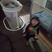 Anthony is registered to the contest to win money with this photo: child, toddler, indoors, motion_blur, low_light, bassinet, baby_basket, crib, bedroom, wood_floor, carpet, furniture, sitting, standing, clothing, green_shirt, dark_room, home, baby用品, candid_photo