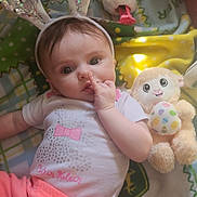 Cadhla joined the competition — help win amazing prizes! baby, bunny_ears, plush_toy, blanket, pink_pants, white_shirt, finger_in_mouth, toy_lamb, decorated_egg, floor_toy, soft_light, child, indoor, cute, headband, face, person, infant, laying_down, playful