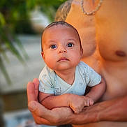 Lenny a rejoint le concours — aidez-le/la à gagner de superbes lots ! baby, infant, child, person, cute, onesie, arms, holding, portrait, face, skin, outdoor, nature, greenery, blurred_background, expression, curious, young, parent, tattoo