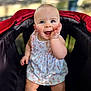 baby, child, stroller, dress, smiling, happy, outdoor, blue_eyes, peach_pattern, hand, cute, infant, person, young, skin, sitting, playful, daylight, portrait, fun