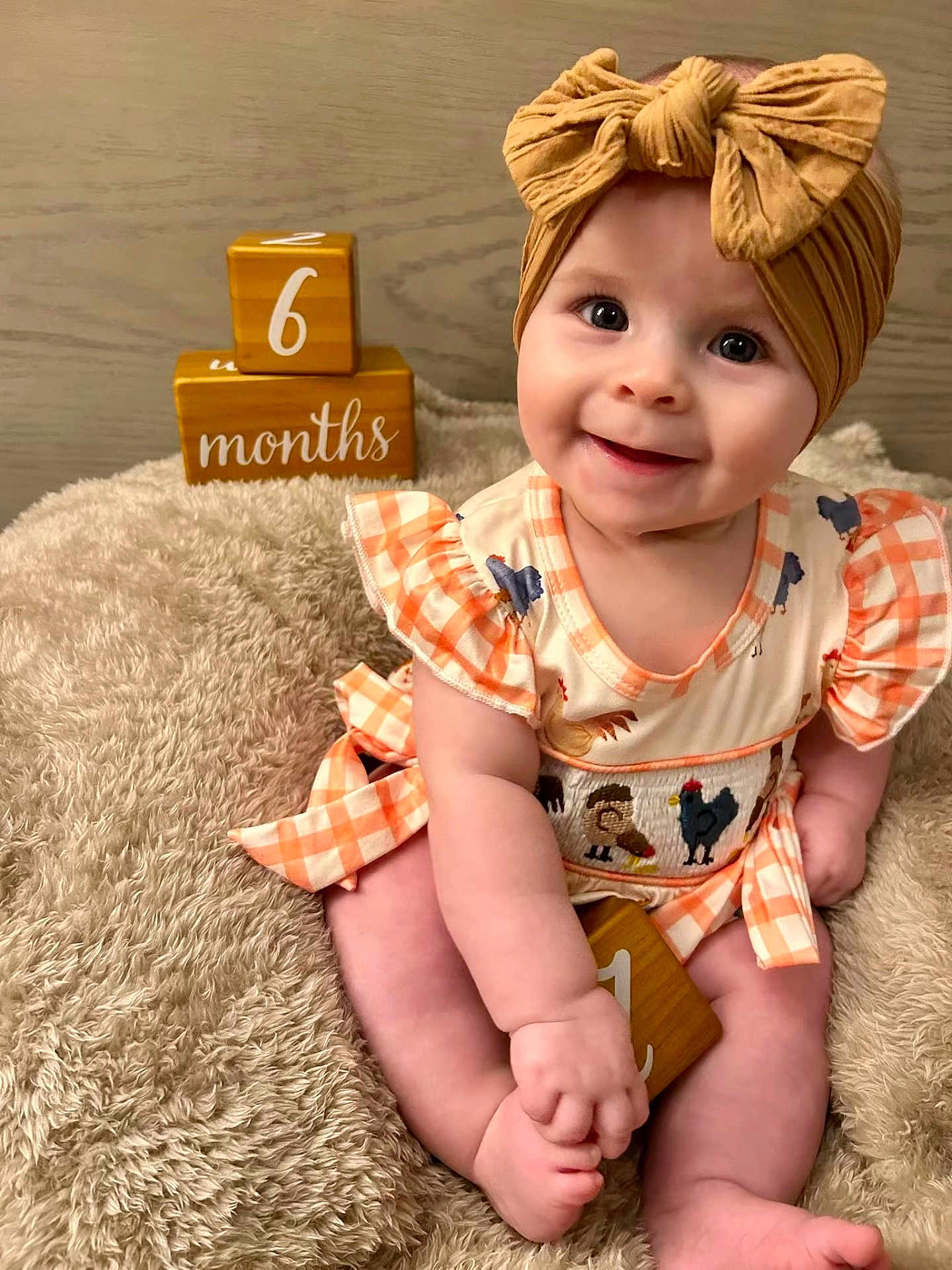 Renley is registered to the contest to win money with this photo: baby, infant, smiling, headband, dress, orange, checkered, wooden_blocks, age_blocks, fluffy_blanket, cute, sitting, indoors, milestone, child, portrait, happy, face, hands, feet