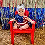 baby, child, red_chair, headband, white_bow, patriotic_outfit, stars_and_stripes, smiling, festive_background, streamers, red, blue, silver, wood_chips, outdoor, happy, sitting, cute, portrait, person