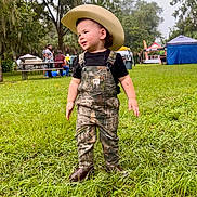 Ryett joined the competition — help win amazing prizes! toddler, child, cowboy_hat, overalls, camouflage, grass, outdoor, people, event, trees, greenery, boots, daytime, nature, smiling, portrait, candid, fun, young_child, festival