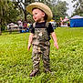 toddler, child, cowboy_hat, overalls, camouflage, grass, outdoor, people, event, trees, greenery, boots, daytime, nature, smiling, portrait, candid, fun, young_child, festival