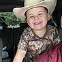 child, smiling, cowboy_hat, camouflage_clothing, car_interior, seat, window, trees, person, happy, portrait, young_child, casual_wear, vehicle, seatbelt, cheerful, face, short_hair, indoor, daylight