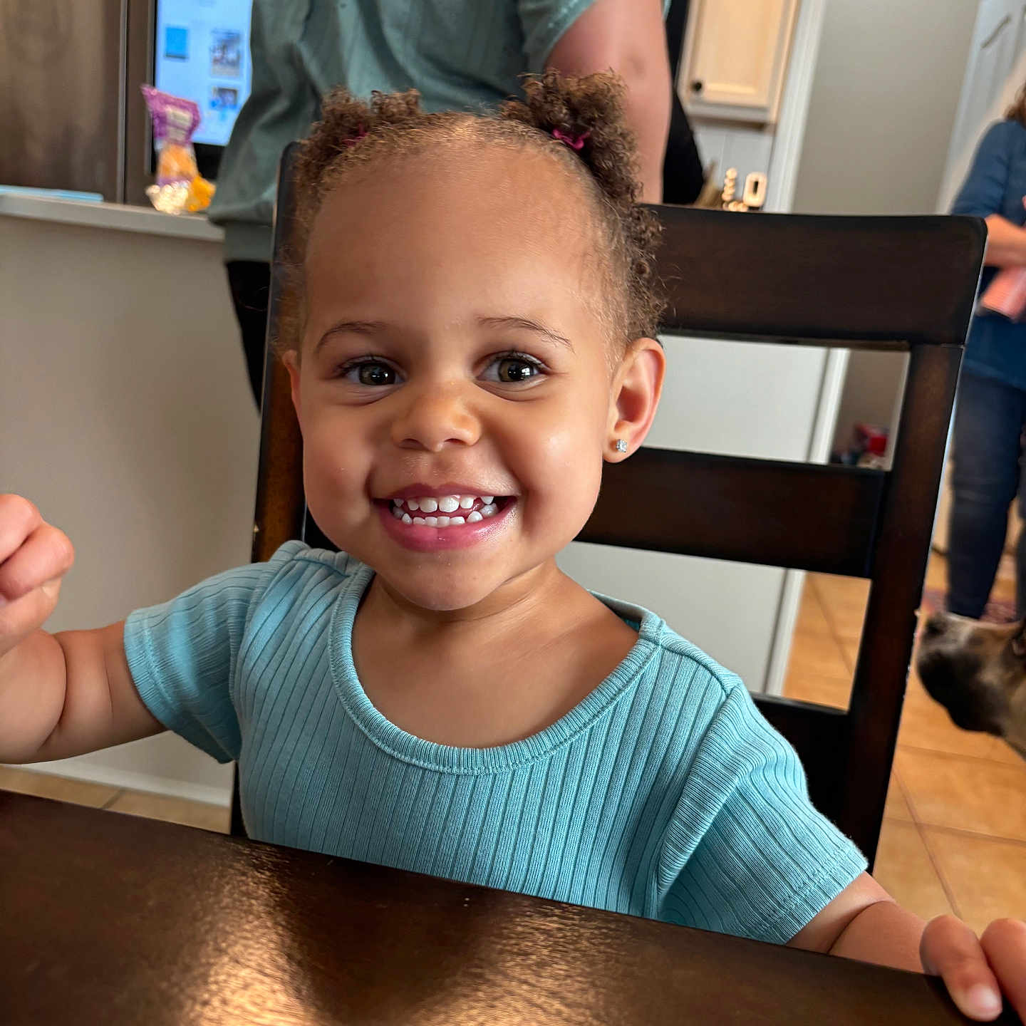 Kamryn is registered to the contest to win money with this photo: adult, background, blue_shirt, chair, child, dog, earrings, hair_pigtails, happy, home, indoor, kitchen, people, person, portrait, smiling, table, tile_floor, toddler, wooden_furniture