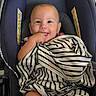 baby, infant, child, smiling, car_seat, blanket, striped_blanket, portrait, indoors, seated, happy, face, hand, chewing, clothing, fabric, safety_seat, vehicle, close_up, casual_photo
