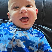Tiberius is registered to the contest to win money with this photo: baby, child, infant, smiling, happy, portrait, face, eyes, mouth, camouflage, blue_clothing, sitting, leather_seat, indoor, home, baby_rocker, furniture, close_up, photography, cheerful